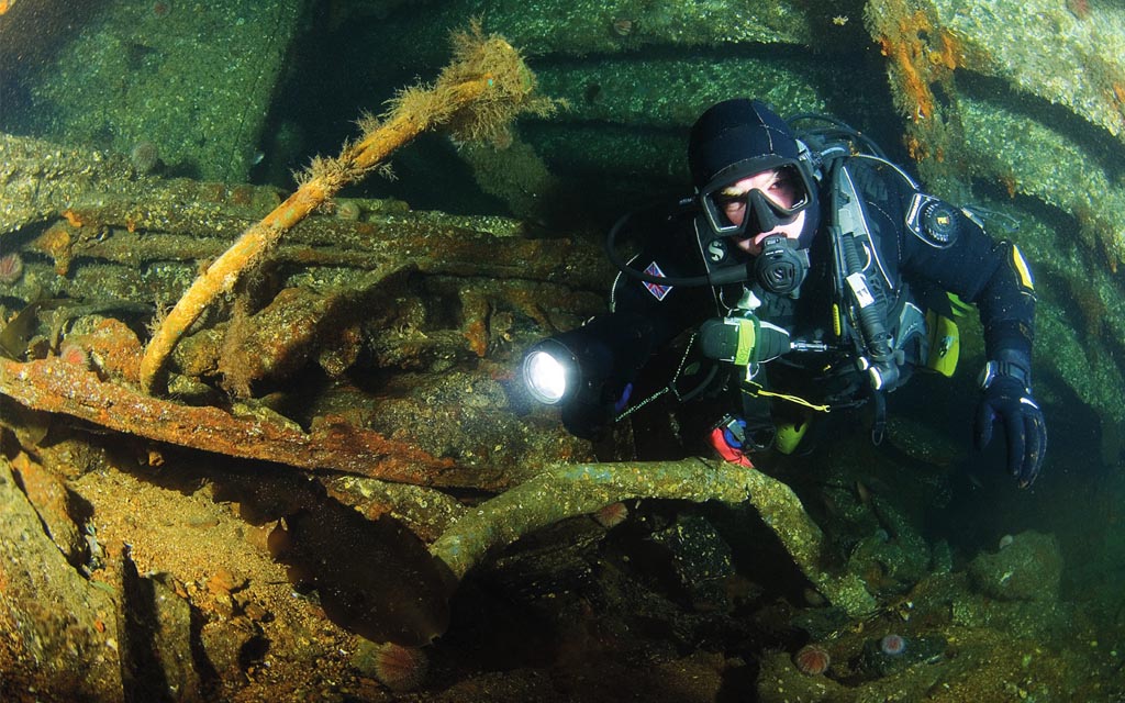 Diver illuminating a wreck with a flashlight