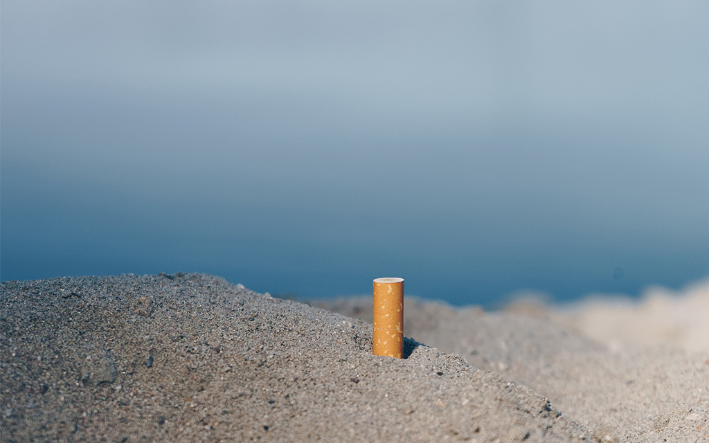 A cigarette butt sticking out of sand at the seaside.