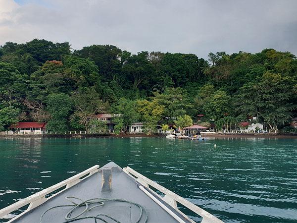 A boat approaches a resort on a densely forested Indonesian coast over emerald green waters 