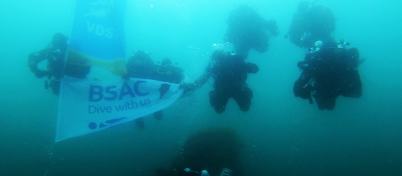 The BSAC and VDST team underwater holding flags of the companies just about the V83 torpedo boat at Scapa Flow