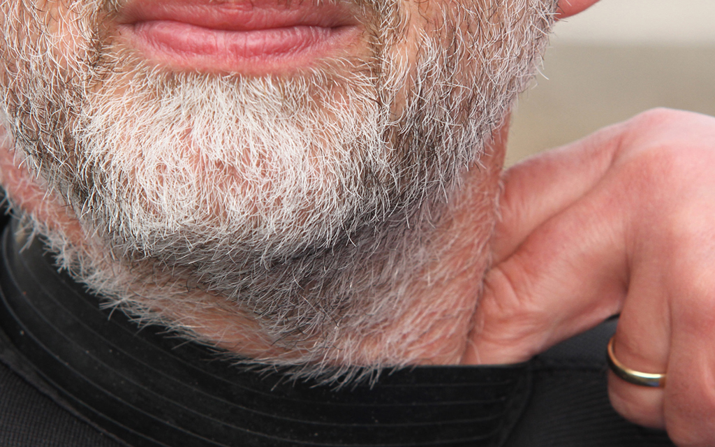 Man with white beard pulling on the latex collar of his dry suit with two fingers