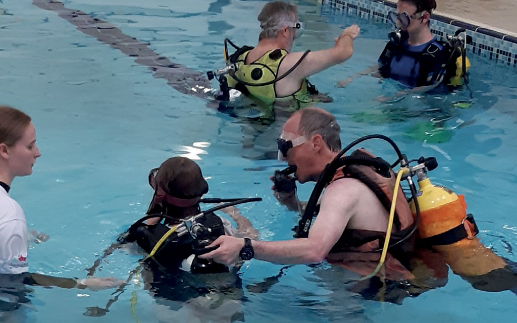 Man helping a young diver on a try dive in a swimming pool