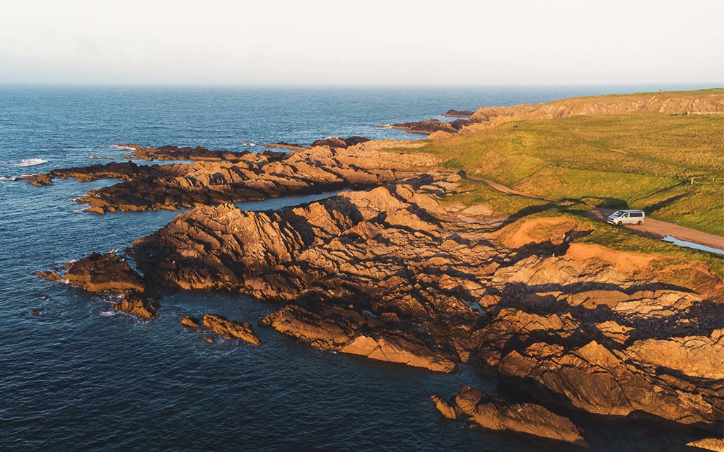 campervan parked near rocks on the shore at golden hour