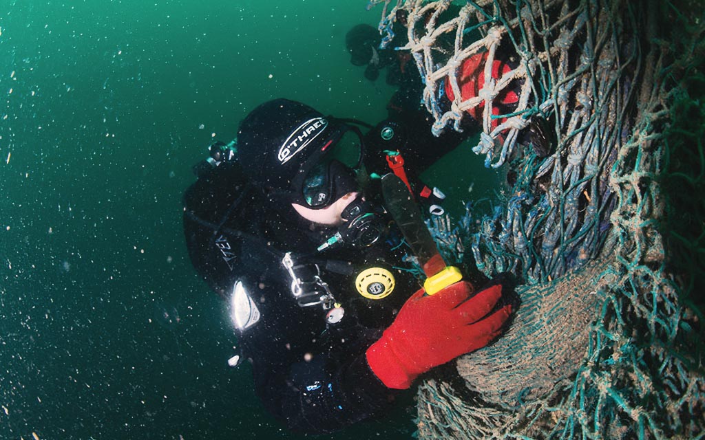 Diver trying to cut loose a net under murky water.