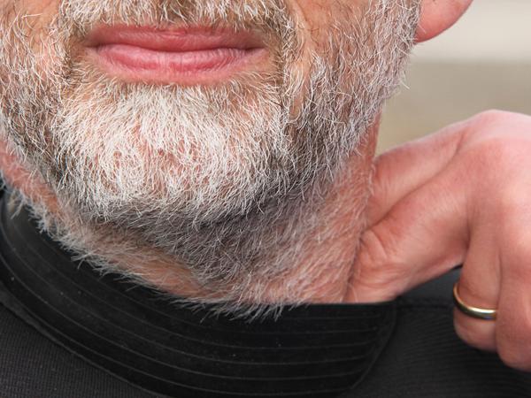 Man with white beard pulling on the latex collar of his dry suit with two fingers