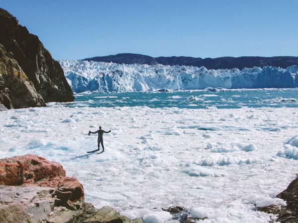 Andy Torbet in a drysuit standing with arms out on ice near a glacier 