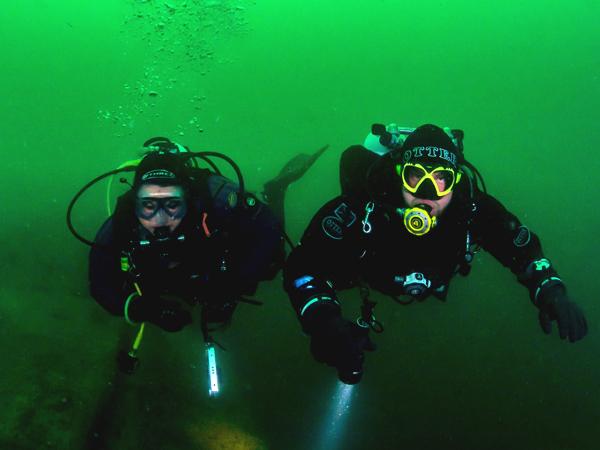 Two scuba divers, mid-dive, illuminated by the flash from the camera. Green, murky waters in the background.