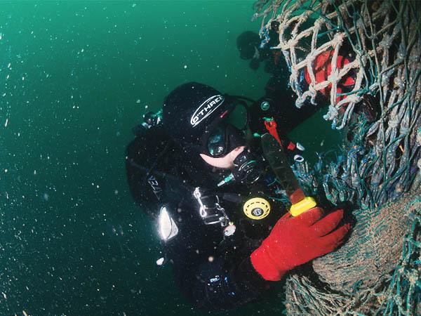 Diver trying to cut loose a net under murky water.