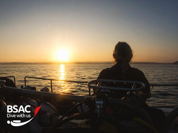 Diver looks out at the sunset from a boat carrying scuba equipment after a long day 