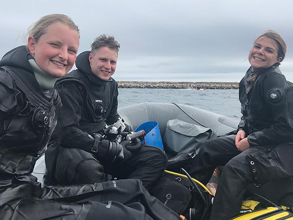 three young scuba divers on a boat smiling 