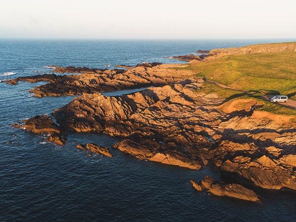 campervan parked near rocks on the shore at golden hour