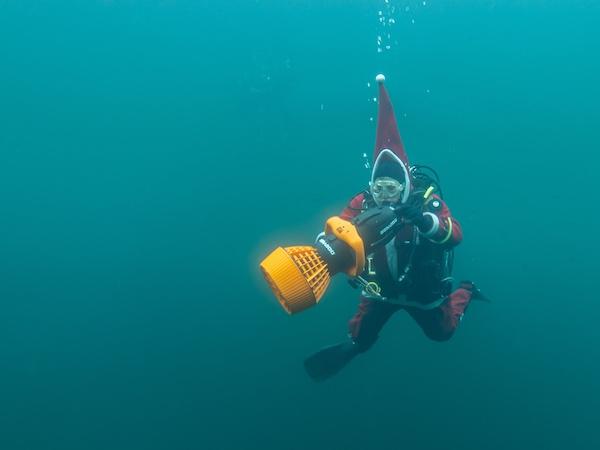 A scuba diver iin a santa costume plays with an underwater scooter