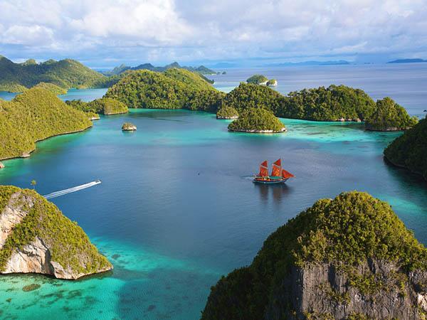 Aerial view of a sailboat in an island cove, surrounded by blue and turquoise water