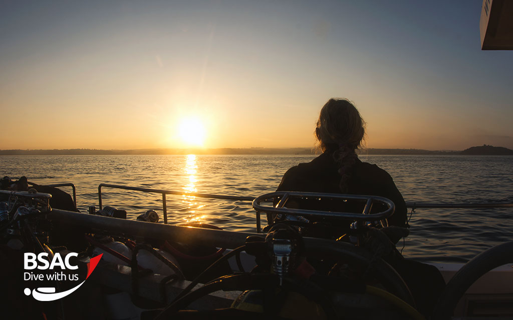 Diver looks out at the sunset from a boat carrying scuba equipment after a long day 