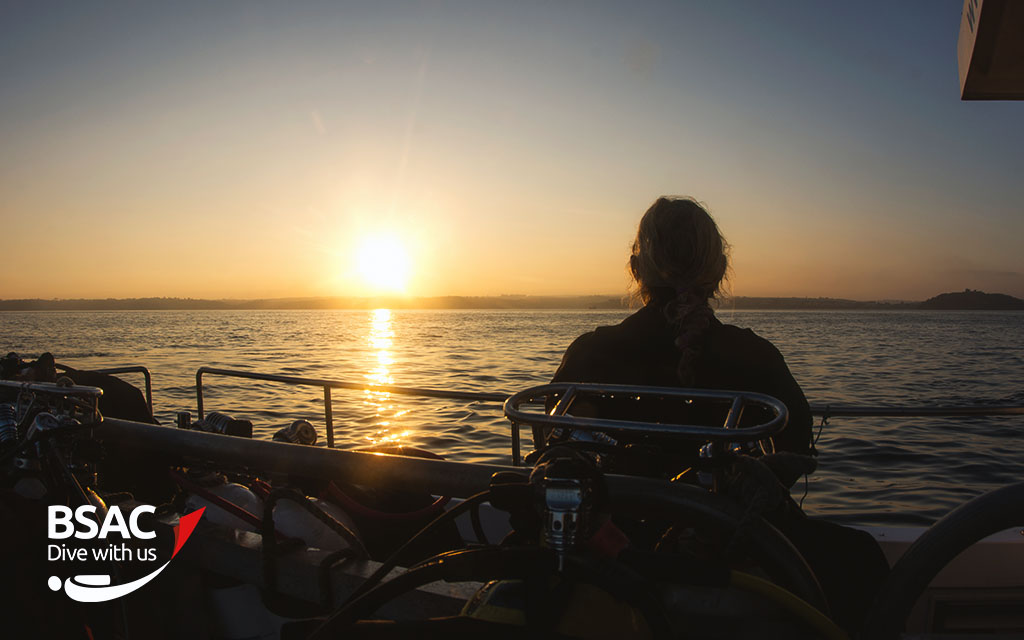 Diver looks out at the sunset from a boat carrying scuba equipment after a long day
