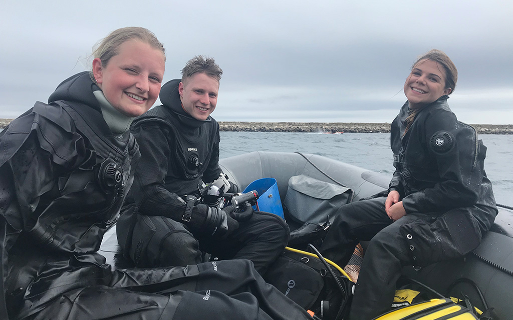 three young scuba divers on a boat smiling 