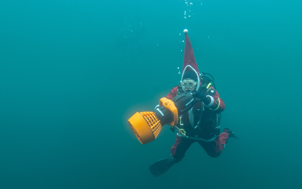 A scuba diver iin a santa costume plays with an underwater scooter