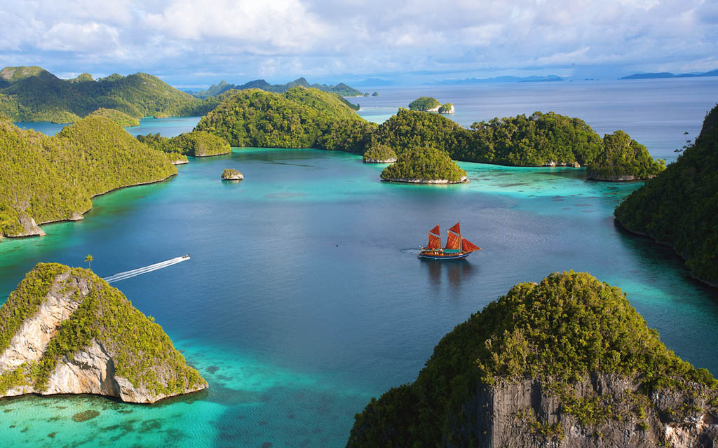 Aerial view of a sailboat in an island cove, surrounded by blue and turquoise water