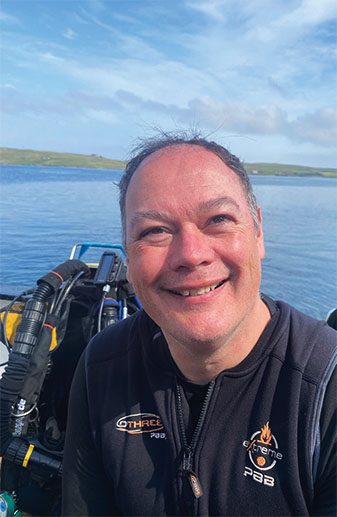 Craig Holdstock, in kit on a boat with blue waters behind him