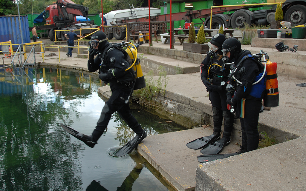 Instructor diver jumping in, trainee divers watching from the side