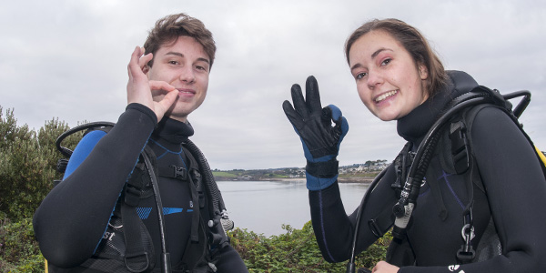 divers on land displaying an okay finger sign to the camera