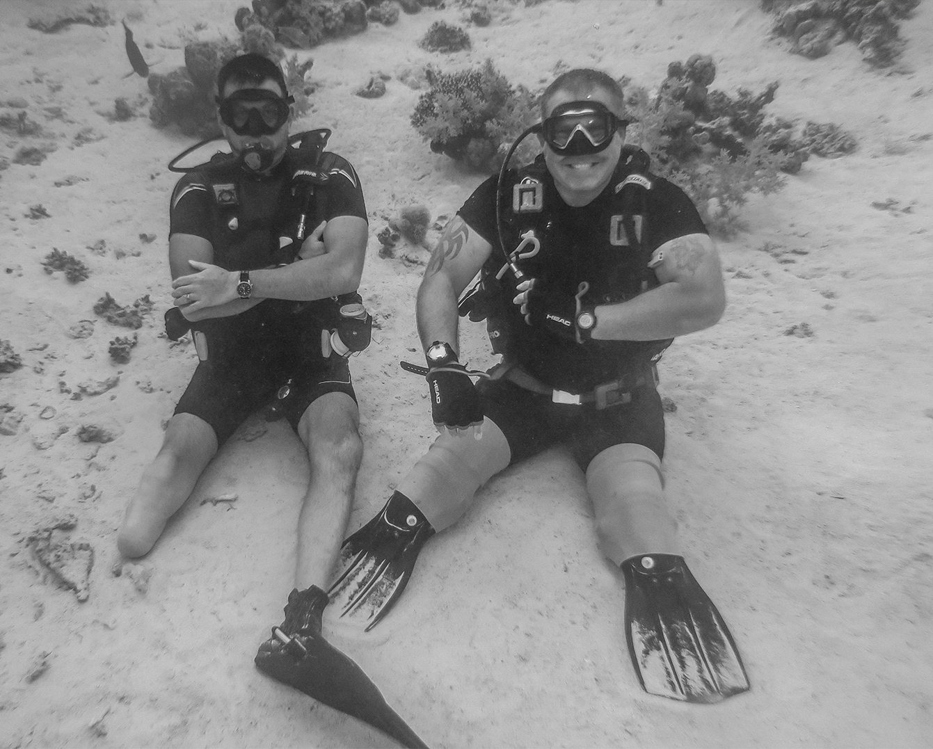 Two divers sat on sandy bottom