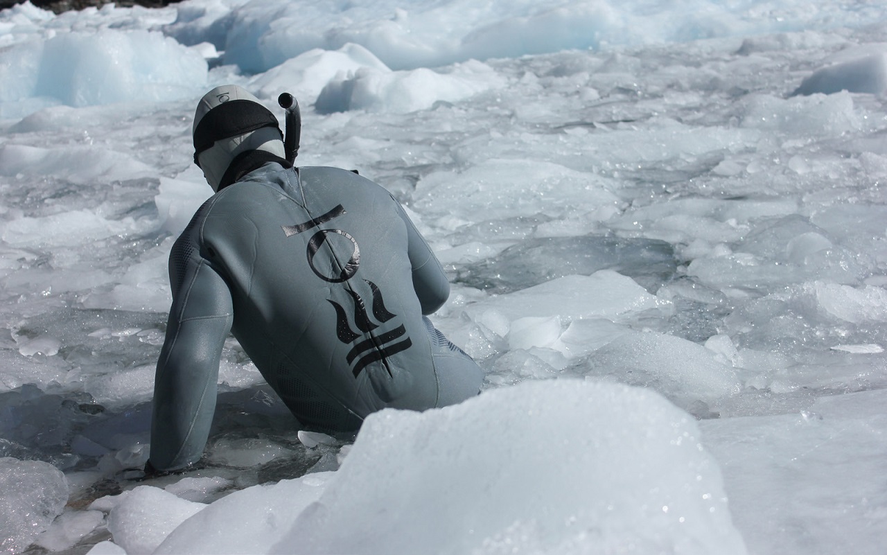 male snorkeller in gray drysuit diving into ice filled water