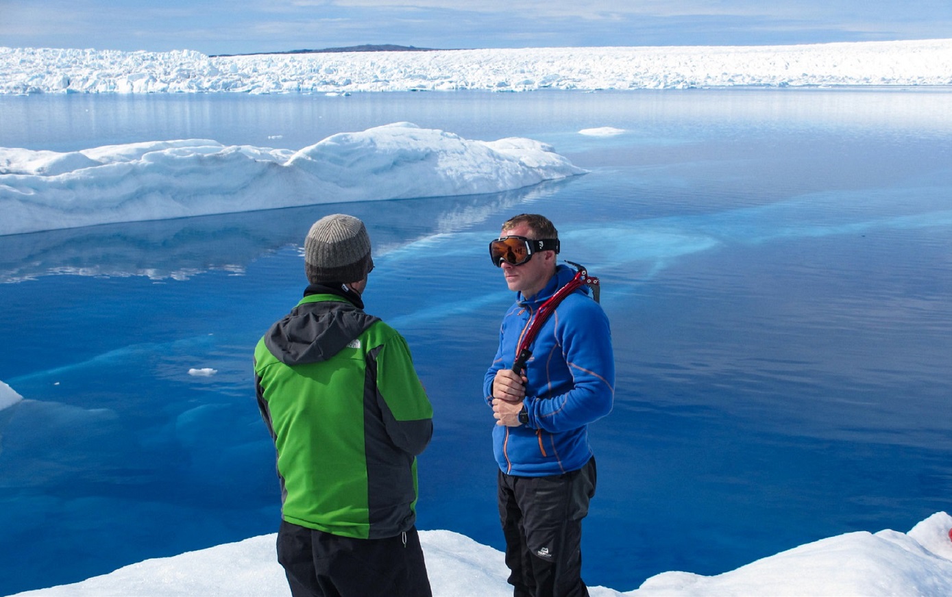 two men conversing on an ice shelf, blue ocean in the backdrop