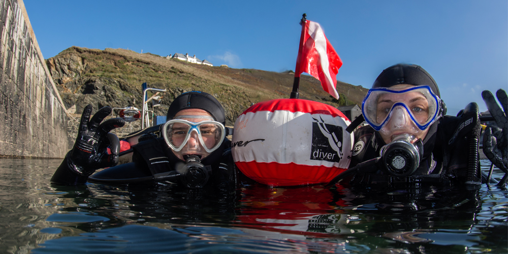 UK pair of divers at surface by a buoy giving ok signals looking to camera